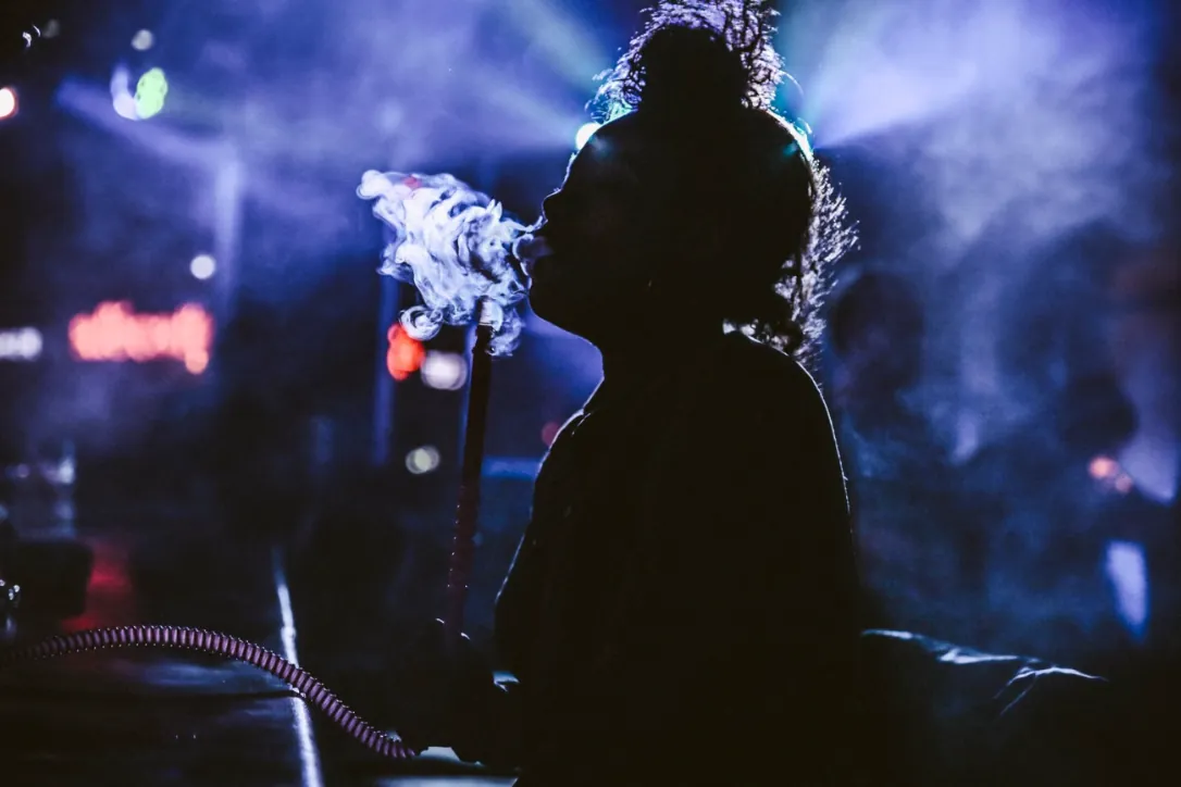 A person exhaling hookah smoke in a dim lounge